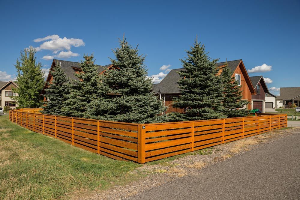A wooden fence surrounds a residential area with houses and trees.