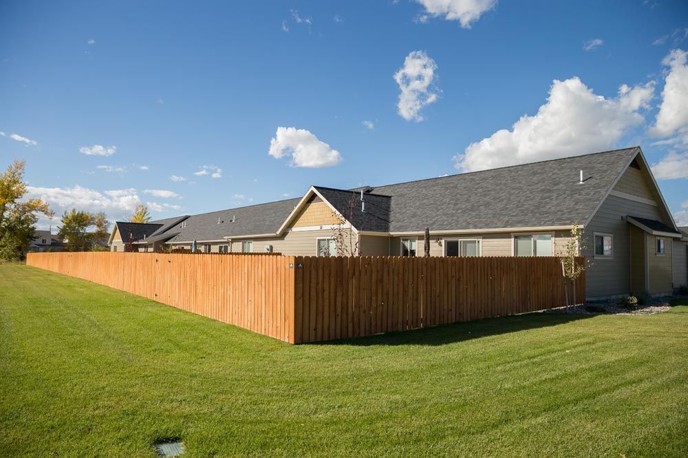 A wooden fence surrounds a lush green lawn in front of a house.
