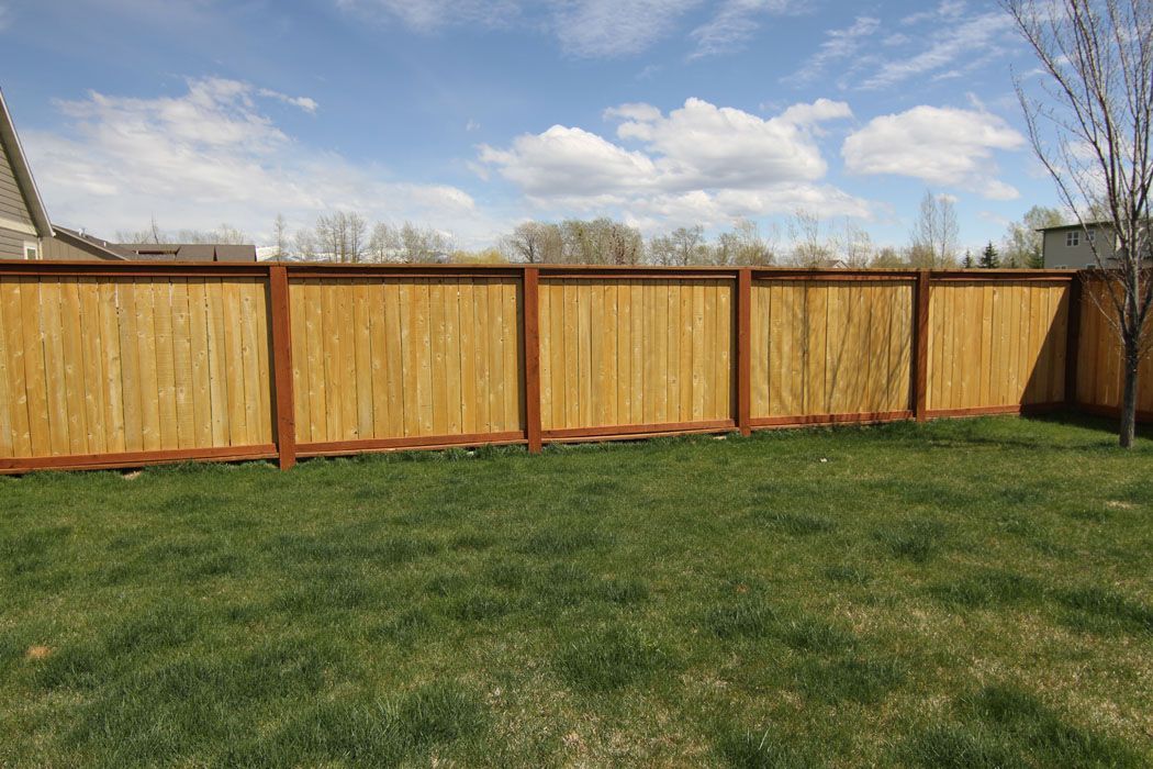 A wooden fence is in the middle of a lush green yard.