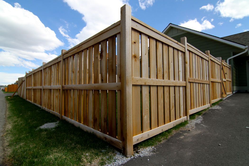 A wooden fence is surrounding a house on a sunny day.