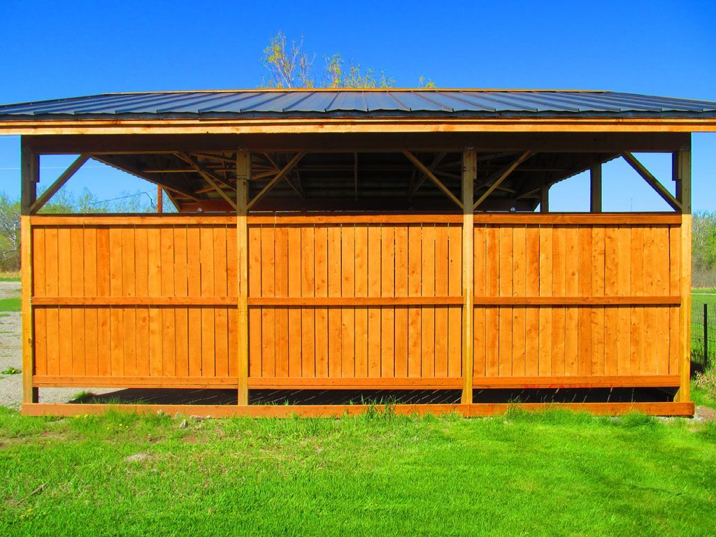 A wooden structure with a metal roof is sitting in the middle of a grassy field.
