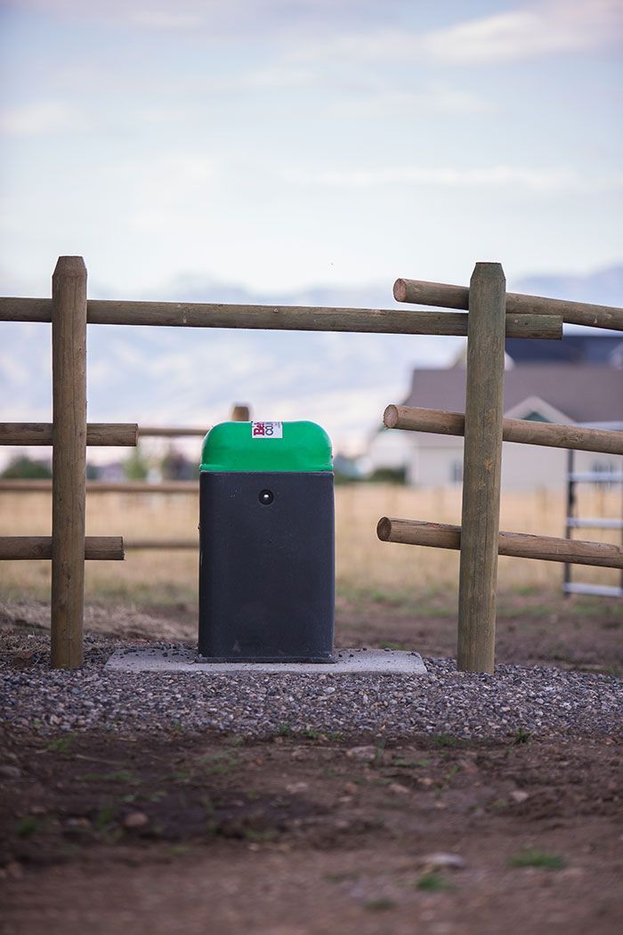 A green trash can is sitting next to a wooden fence.