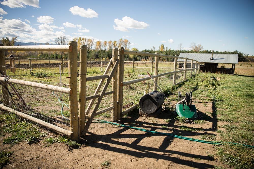 A wooden fence with a gate and a hose in a field.