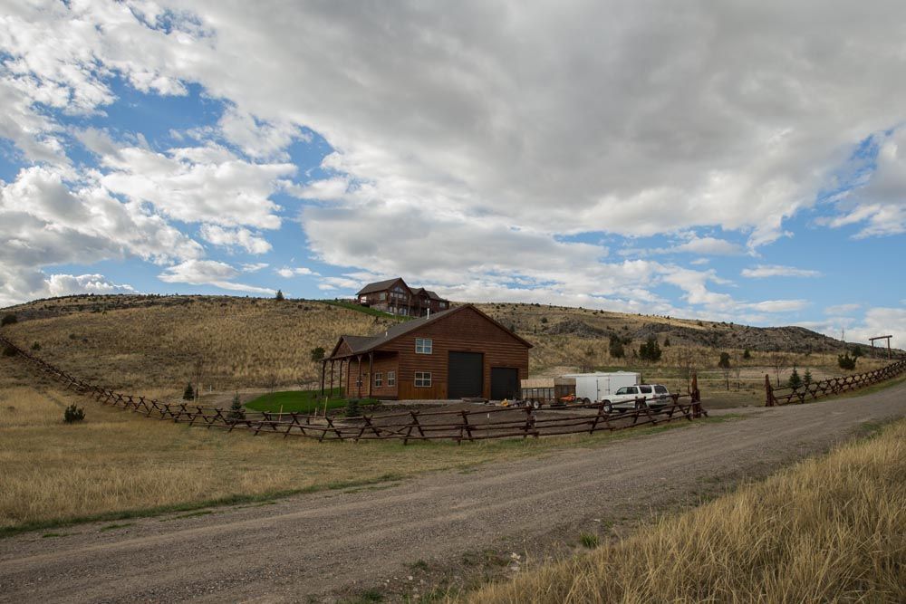 A barn is sitting on top of a hill next to a dirt road.