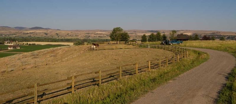 A dirt road going through a field with a wooden fence.