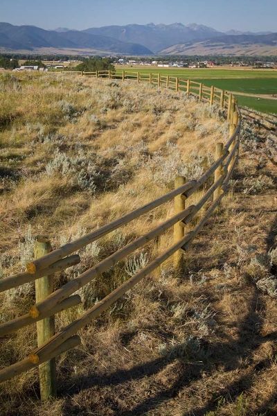 A wooden fence surrounds a dry grass field with mountains in the background.