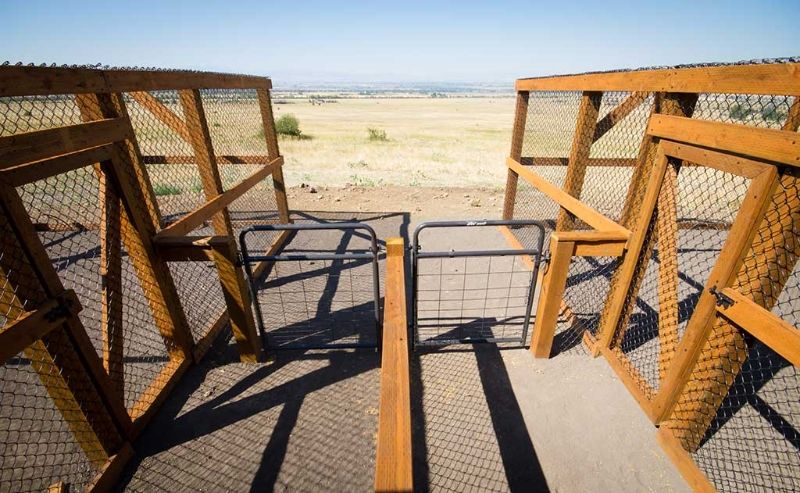 A wooden fence with a metal gate leading to a field.