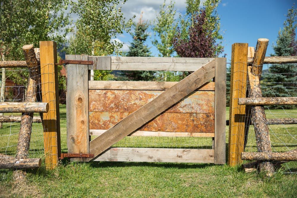 A wooden fence with a wooden gate in the middle of a grassy field.