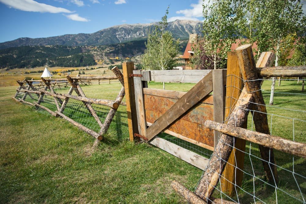 A wooden fence surrounds a grassy field with mountains in the background.