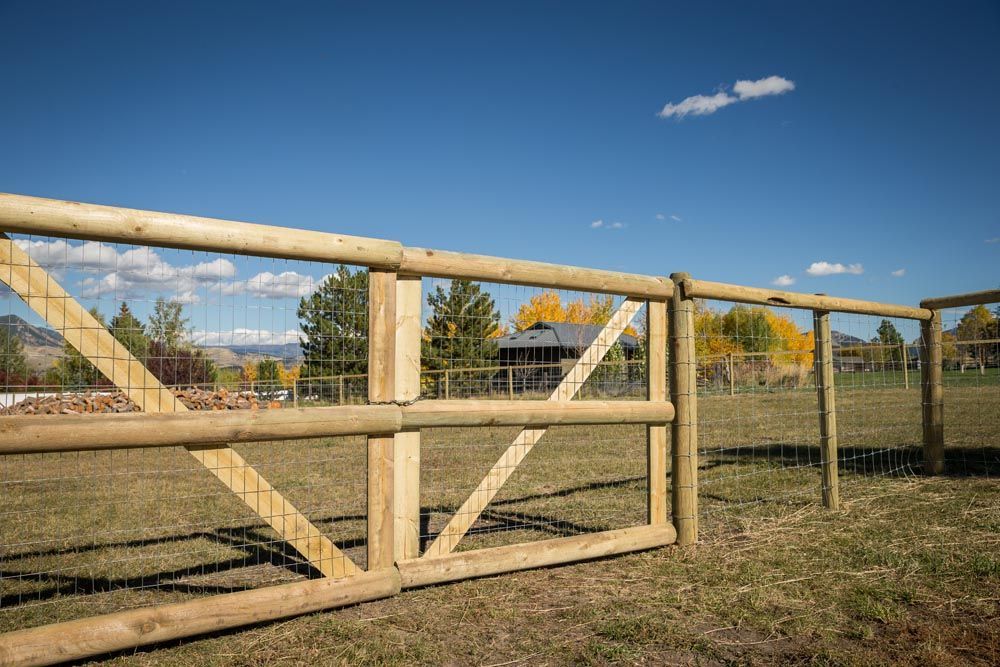 A wooden fence with a gate in the middle of a grassy field.