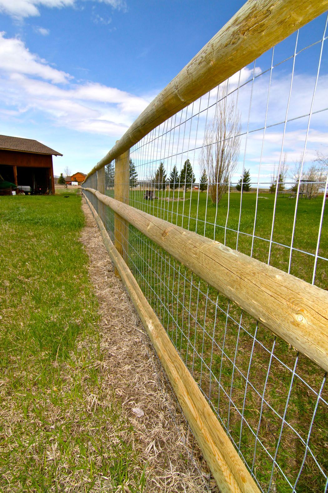 A wooden fence surrounds a grassy field with a barn in the background.
