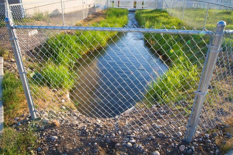 A chain link fence surrounds a small stream.