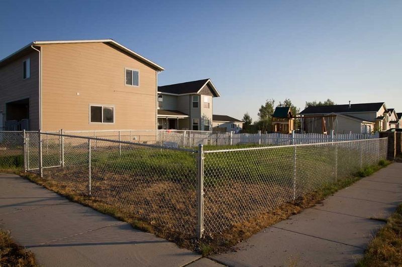 A chain link fence surrounds an empty lot in front of a house.