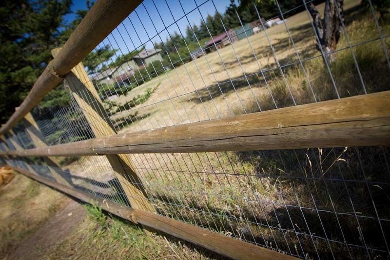 A wooden fence with a wire fence surrounding a field.