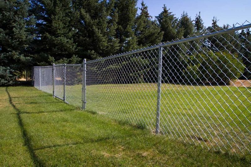 A chain link fence surrounds a lush green field.