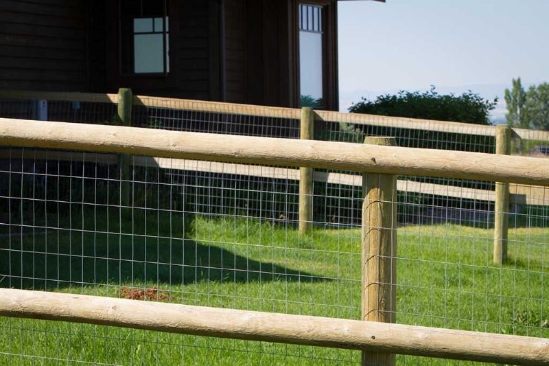 A wooden fence with a wire fence in front of a house.
