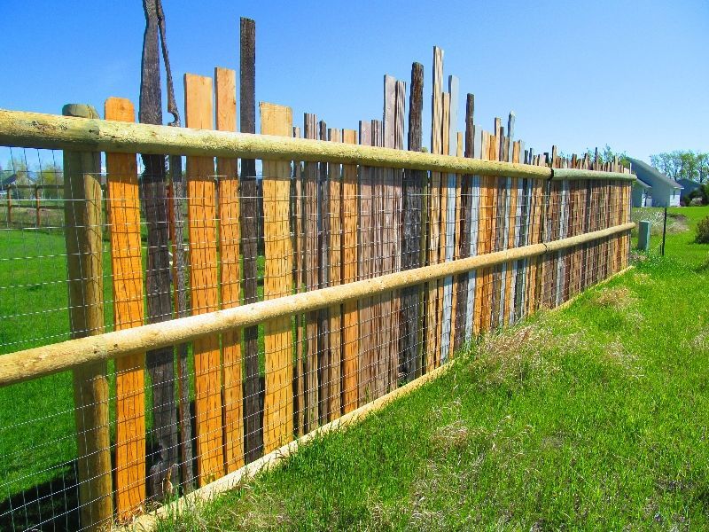 A wooden fence is surrounded by a wire fence in a grassy field.