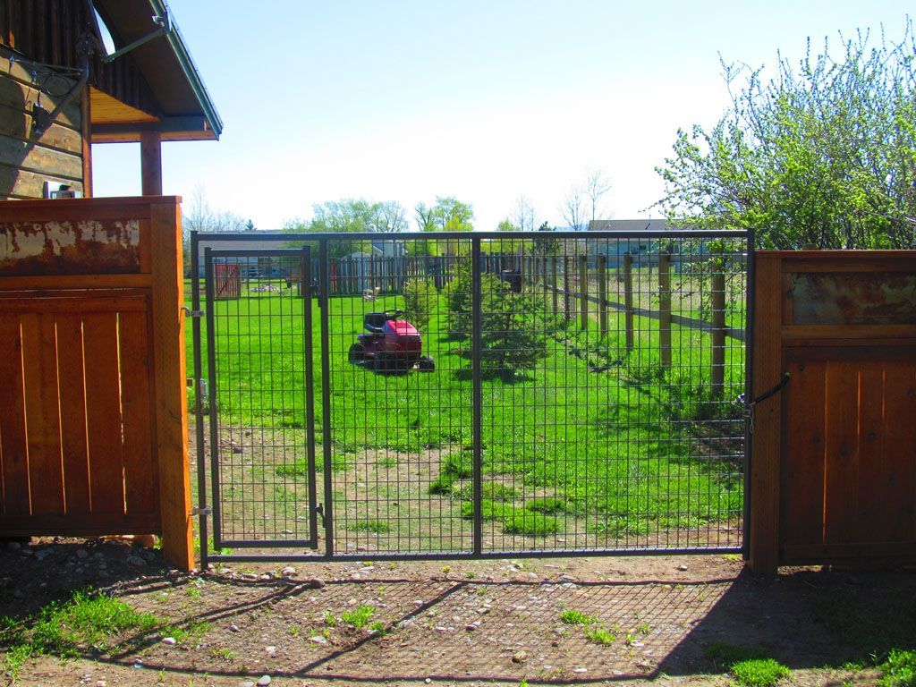 A red car is parked in the grass behind a gate.