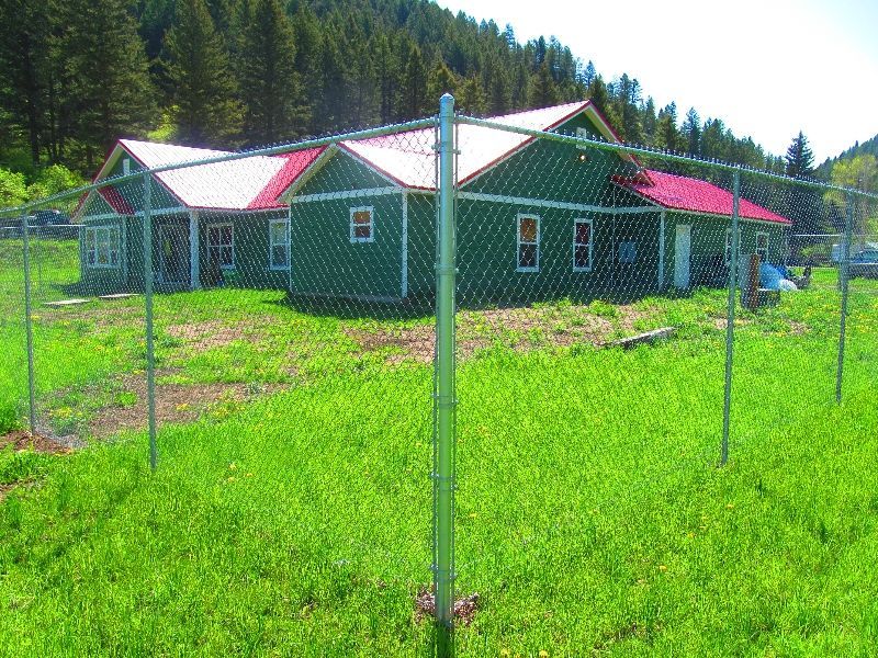A green house with a red roof is behind a chain link fence.