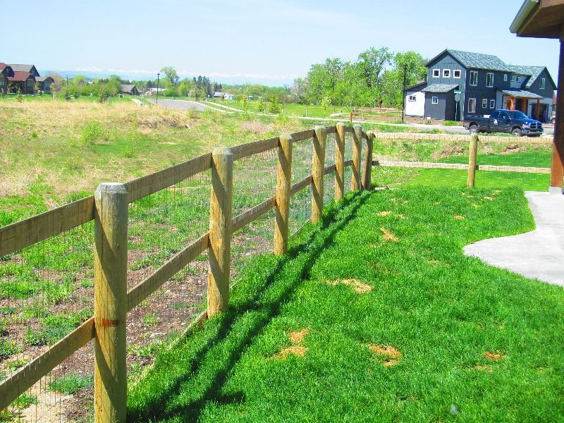 A wooden fence in a grassy field with a house in the background.