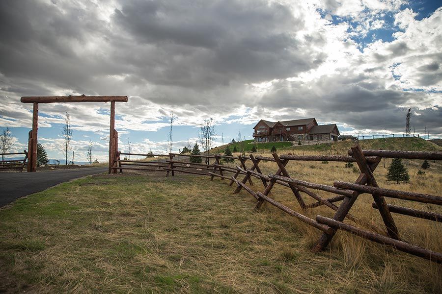 A wooden fence surrounds a grassy field with a house in the background.