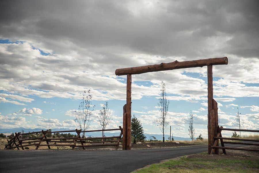 A wooden gate is sitting on the side of a road next to a fence.