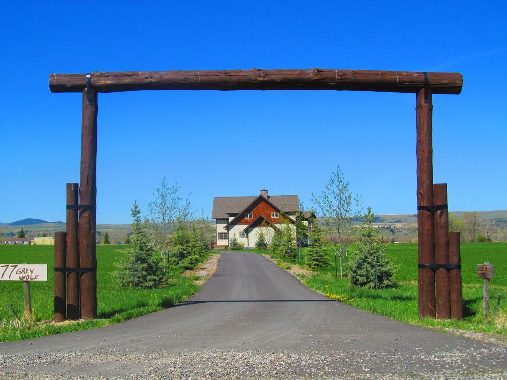 A wooden archway over a road leading to a house.