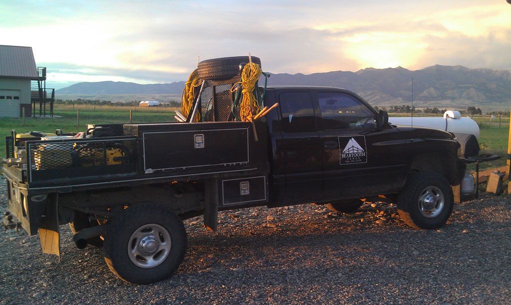 A black truck is parked in a gravel lot with mountains in the background.