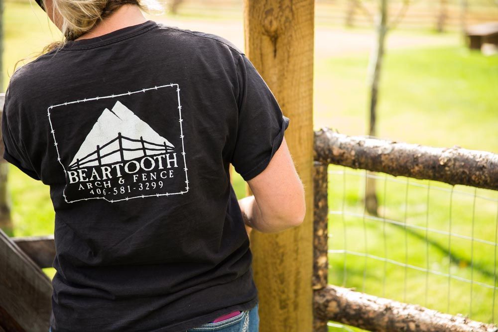 A woman in a black shirt is standing next to a wooden fence.