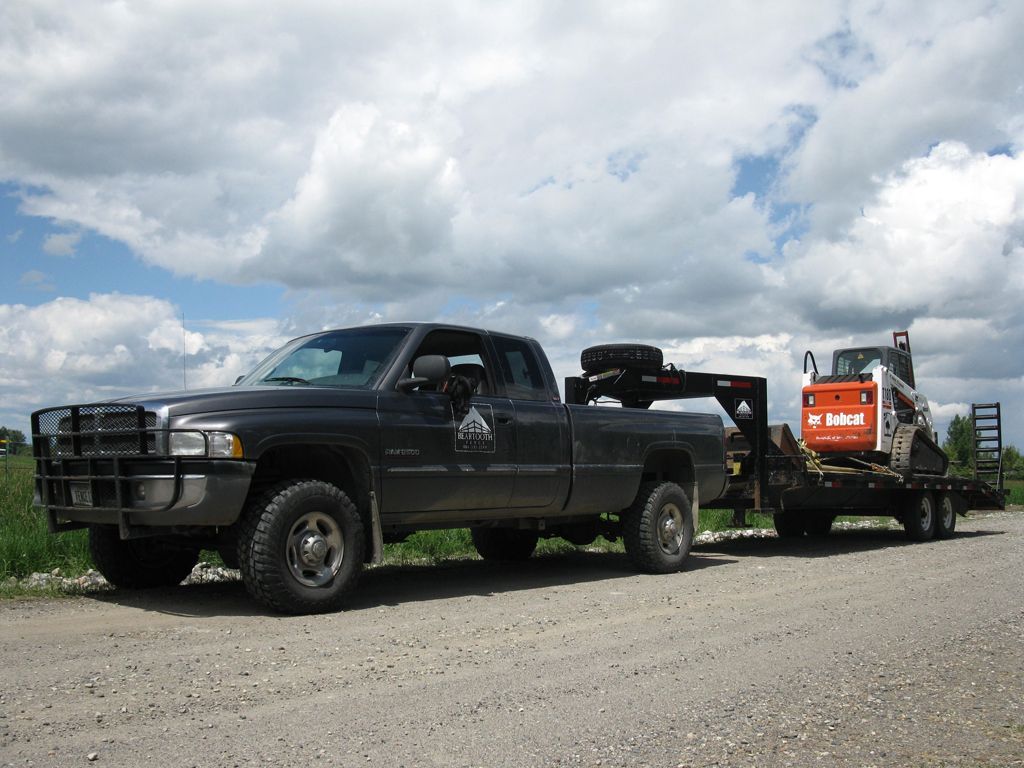 A black truck is towing a bobcat on a trailer.