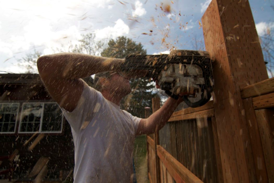 A man is using a chainsaw to cut a wooden fence post.