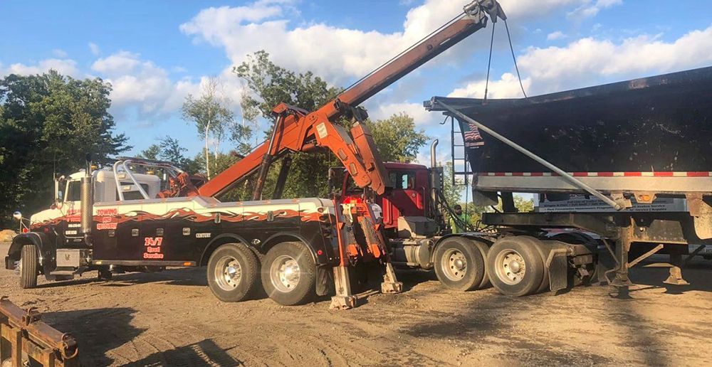 Tow truck lifting the front of a trailer on a gravel lot under a blue sky.