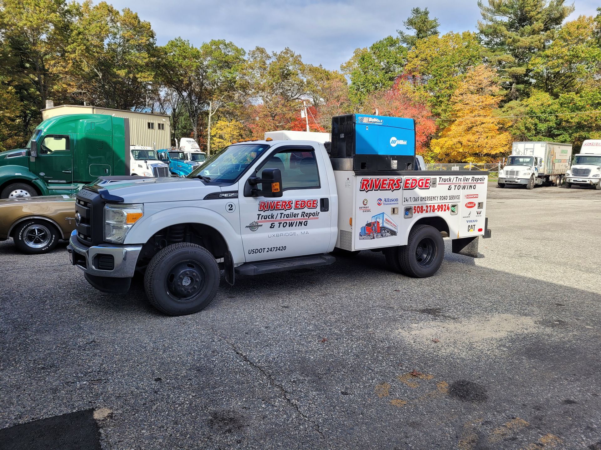 White work truck with a welder in a parking lot, trees in background.