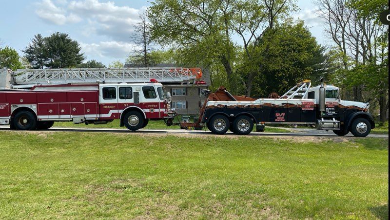 Fire truck and tow truck parked on a grassy roadside. Red and white fire truck. Black and white tow truck.