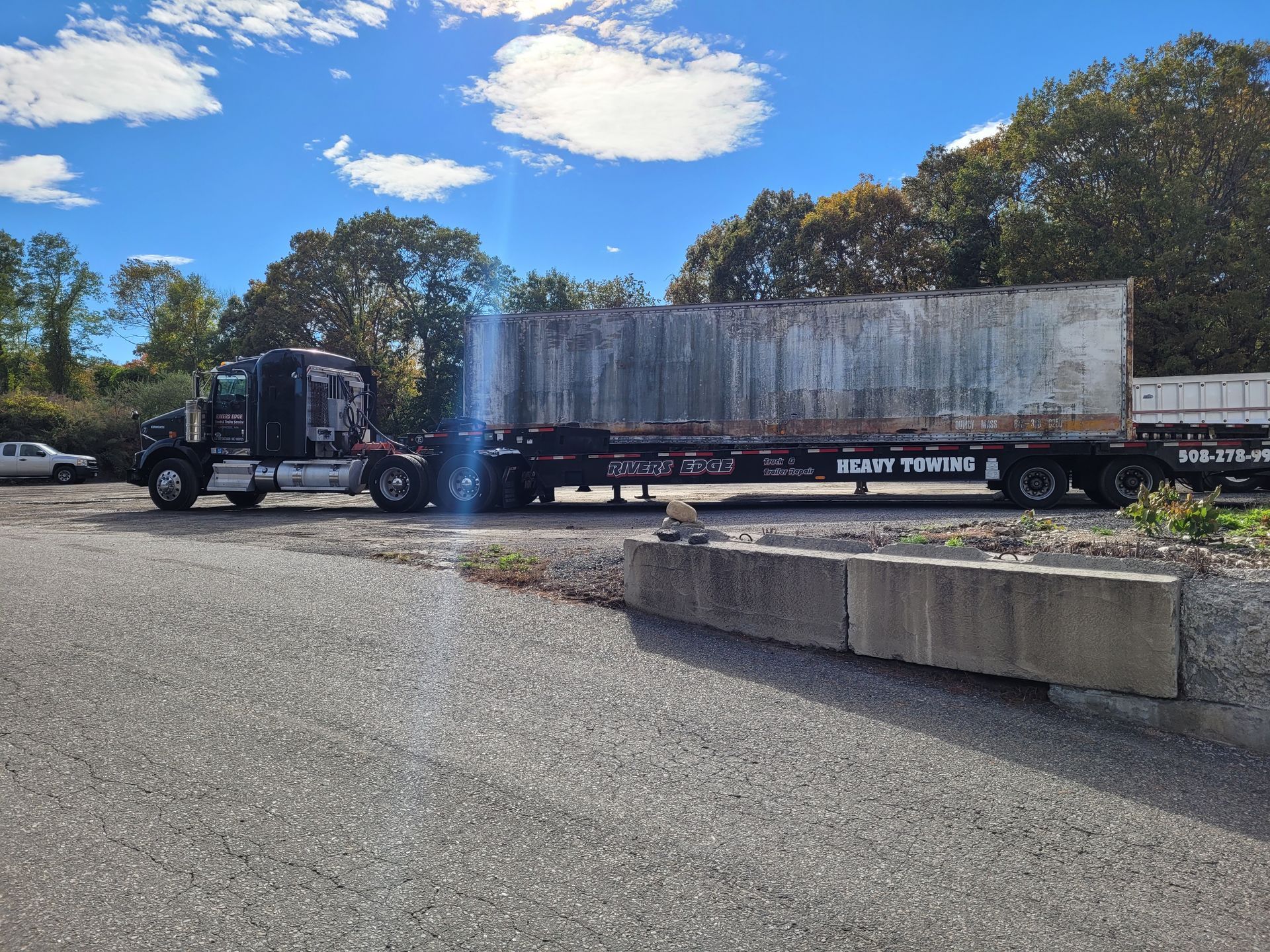 Black semi-truck hauling a large, rectangular metal container on a flatbed trailer, parked outdoors.
