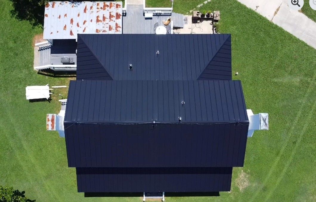 Overhead view of a dark blue-roofed building with green grass surrounding it. Another roof is visible to the left.