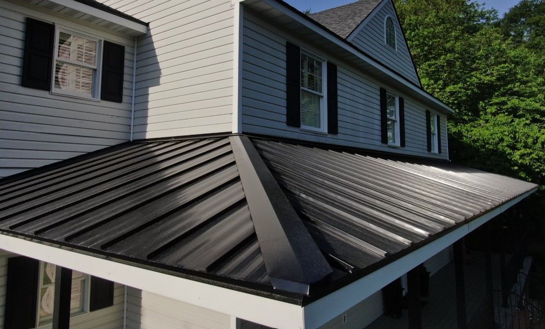 Two-story house with black metal roof and gray siding, black shutters on windows.