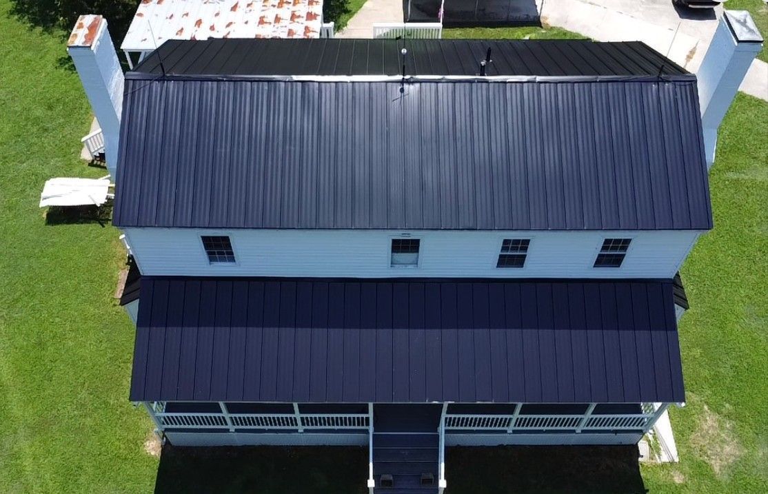 Overhead view of a two-story white house with a black metal roof, chimneys, and a front porch.