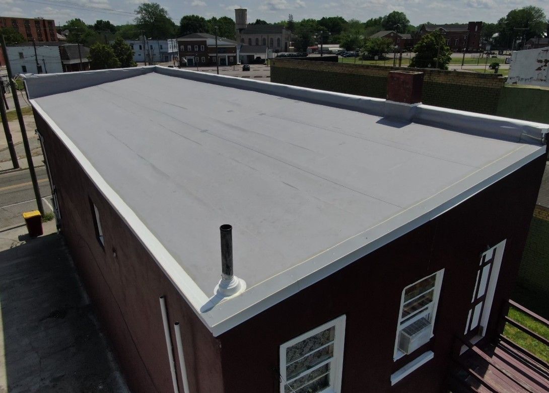 View of a low-rise, brown brick building with a flat, light gray roof and white trim in a town setting.