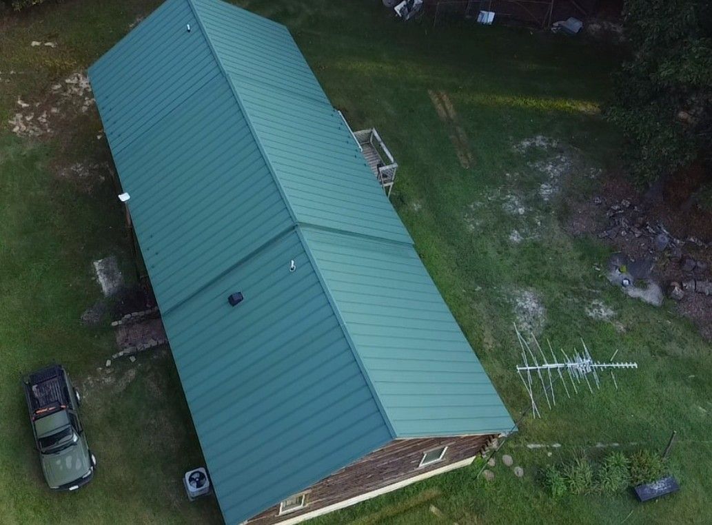 Overhead view of a long green-roofed building on a grassy lot, with a vehicle parked nearby.