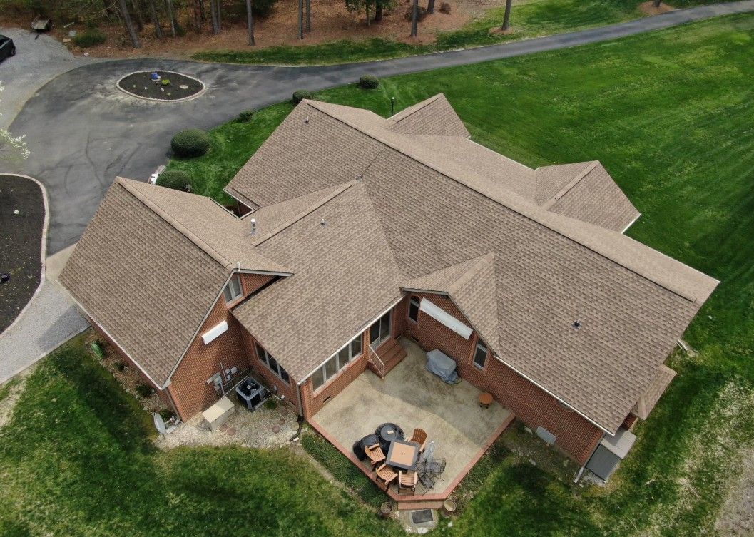 Brown-roofed brick house with a patio, surrounded by green grass and a paved driveway.