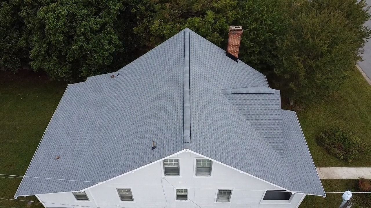 Overhead view of a white house with a gray roof and a brick chimney, surrounded by green trees and grass.