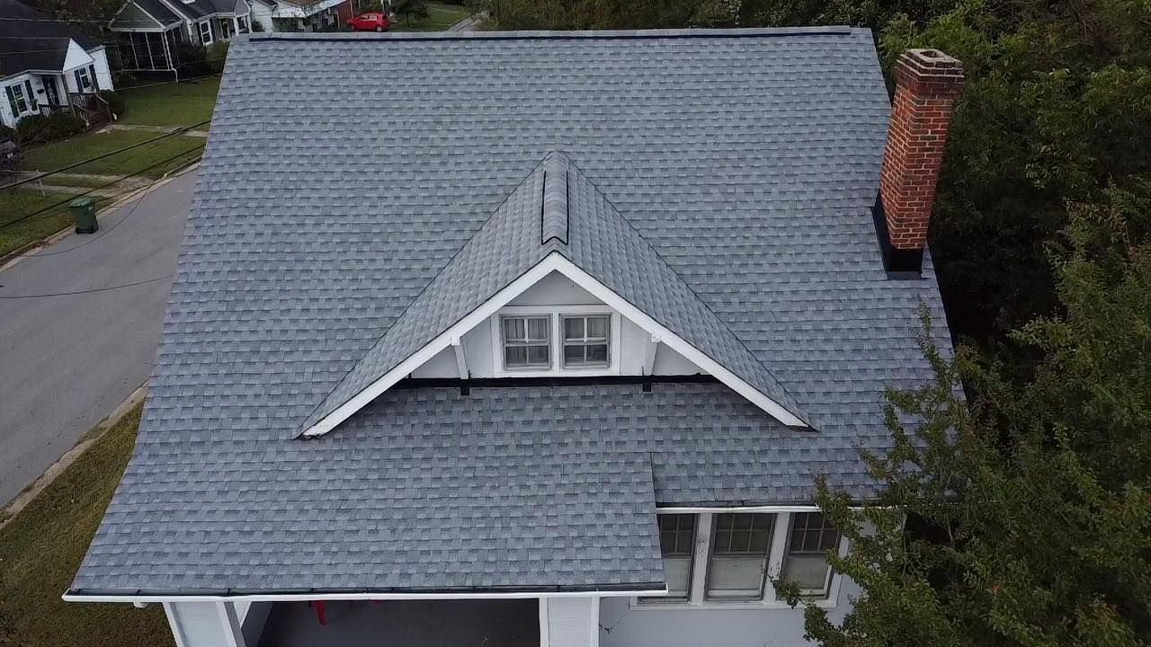 Gray roof of a two-story house with a white gable and brick chimney.