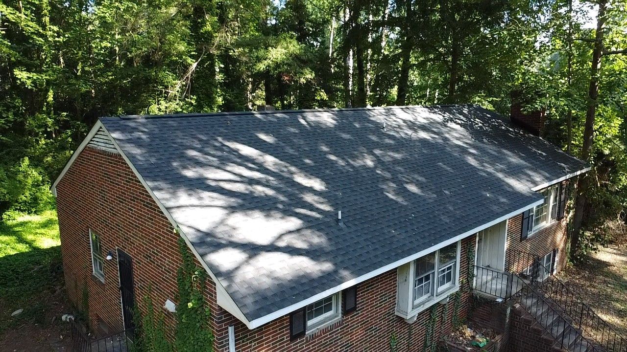 Brick house with dark roof surrounded by trees.
