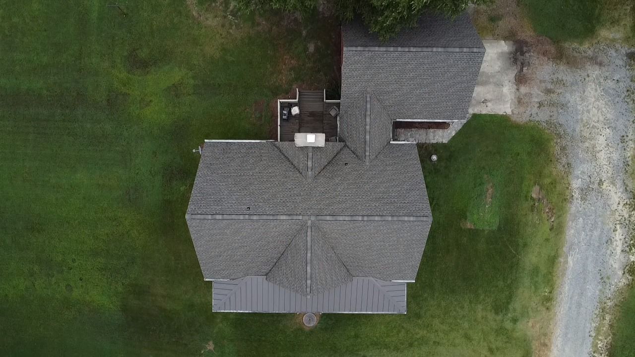 Overhead view of a house with a gray roof, set on a green lawn with a gravel driveway.