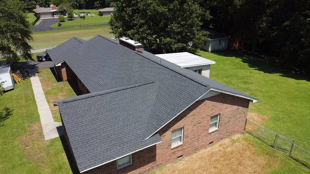 Bird's-eye view of a long, brick building with a dark gray roof on a green lawn.