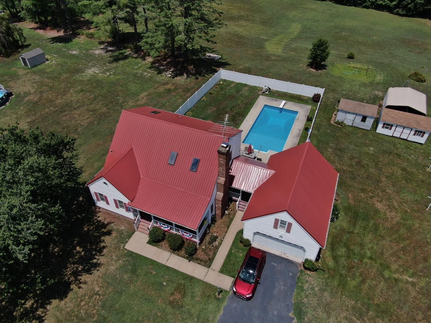 Aerial view of a house with a red roof, a pool, and a car in the driveway on a sunny day.