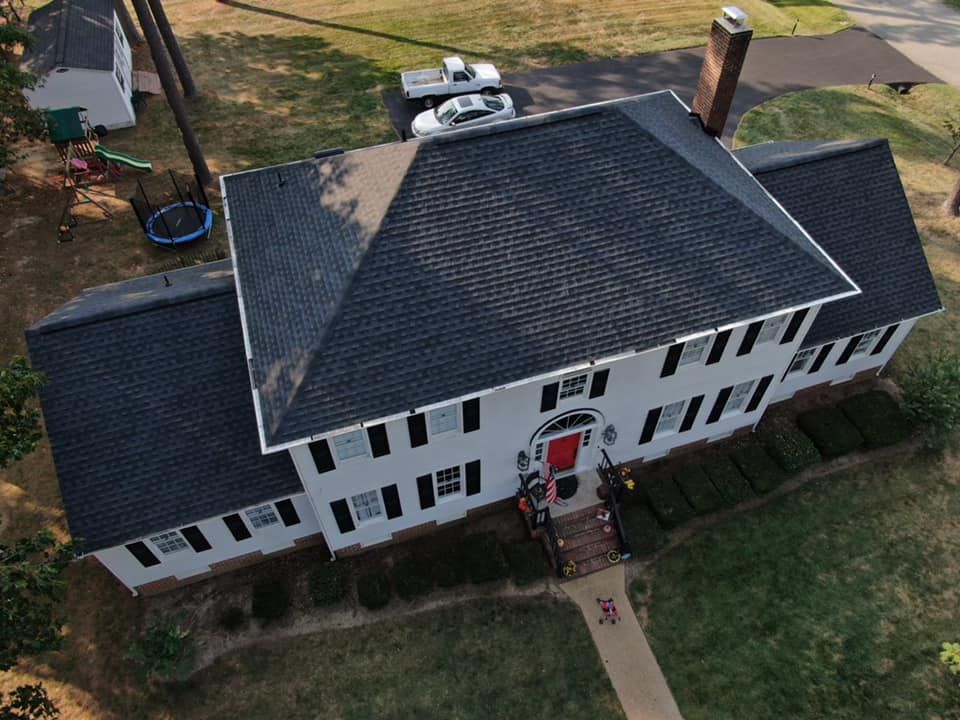 An aerial view of a two-story gray house with a dark gray roof. A driveway and lawn are in front.
