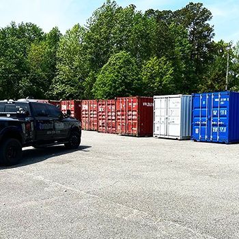 A truck is parked in a parking lot next to a row of shipping containers.