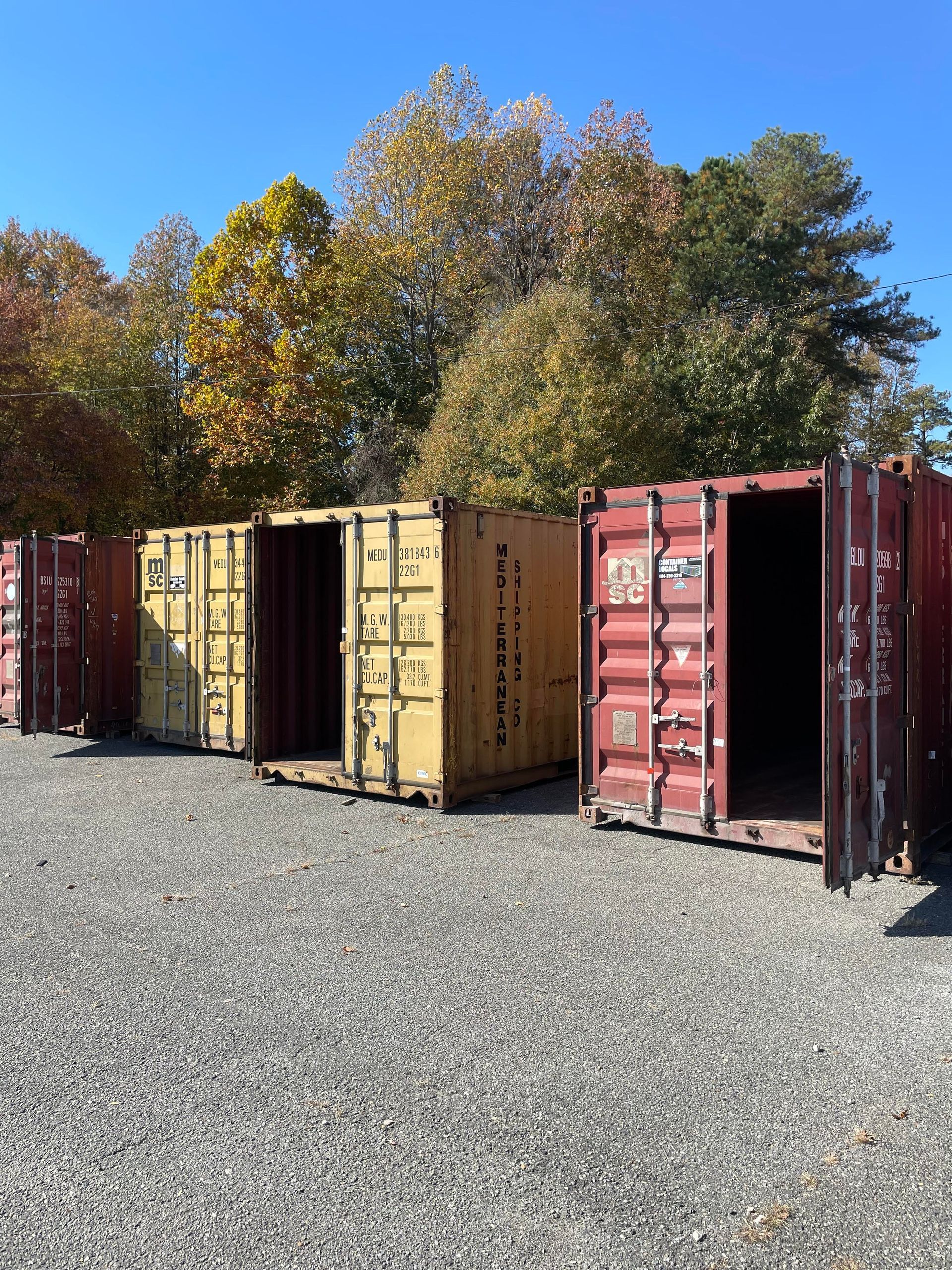 A row of shipping containers are lined up in a gravel lot.